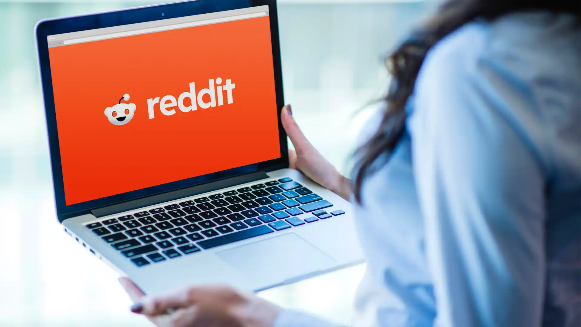 Uma mulher empresária segurando um notebook com um papel de parede da logo do Reddit